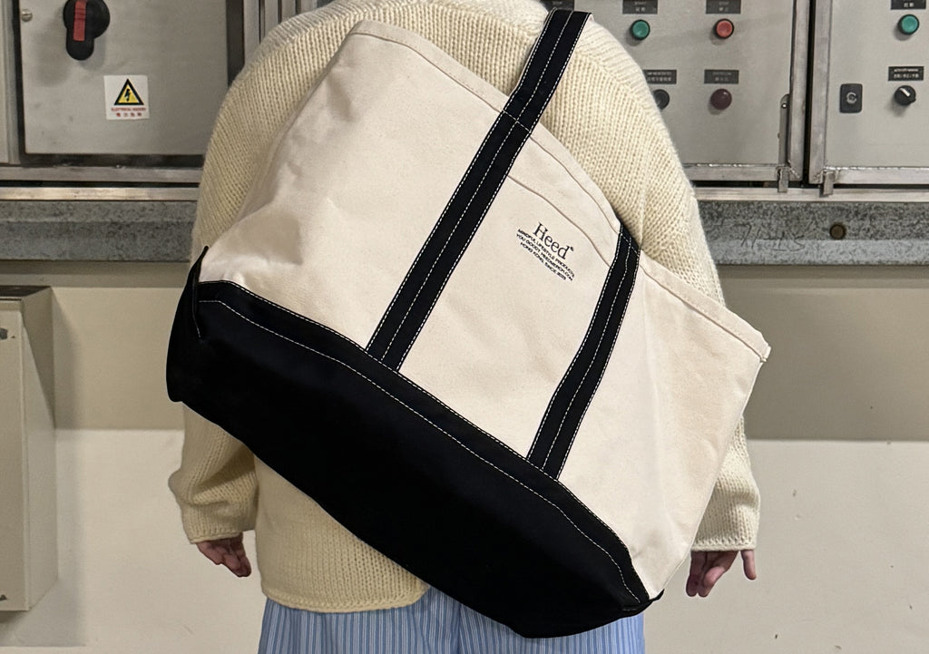 Heed Timeless Boat Tote - Premium Canvas Beach & Travel Bag:  Overhead view of the Heed Timeless Boat Tote in natural cotton canvas. The image highlights the premium 22oz canvas construction, reinforced double-layer base, and overlapped, double-stitched seams for exceptional durability. The shoulder-use handles and subtle black accents are also visible, showcasing the tote's classic, yet contemporary design.